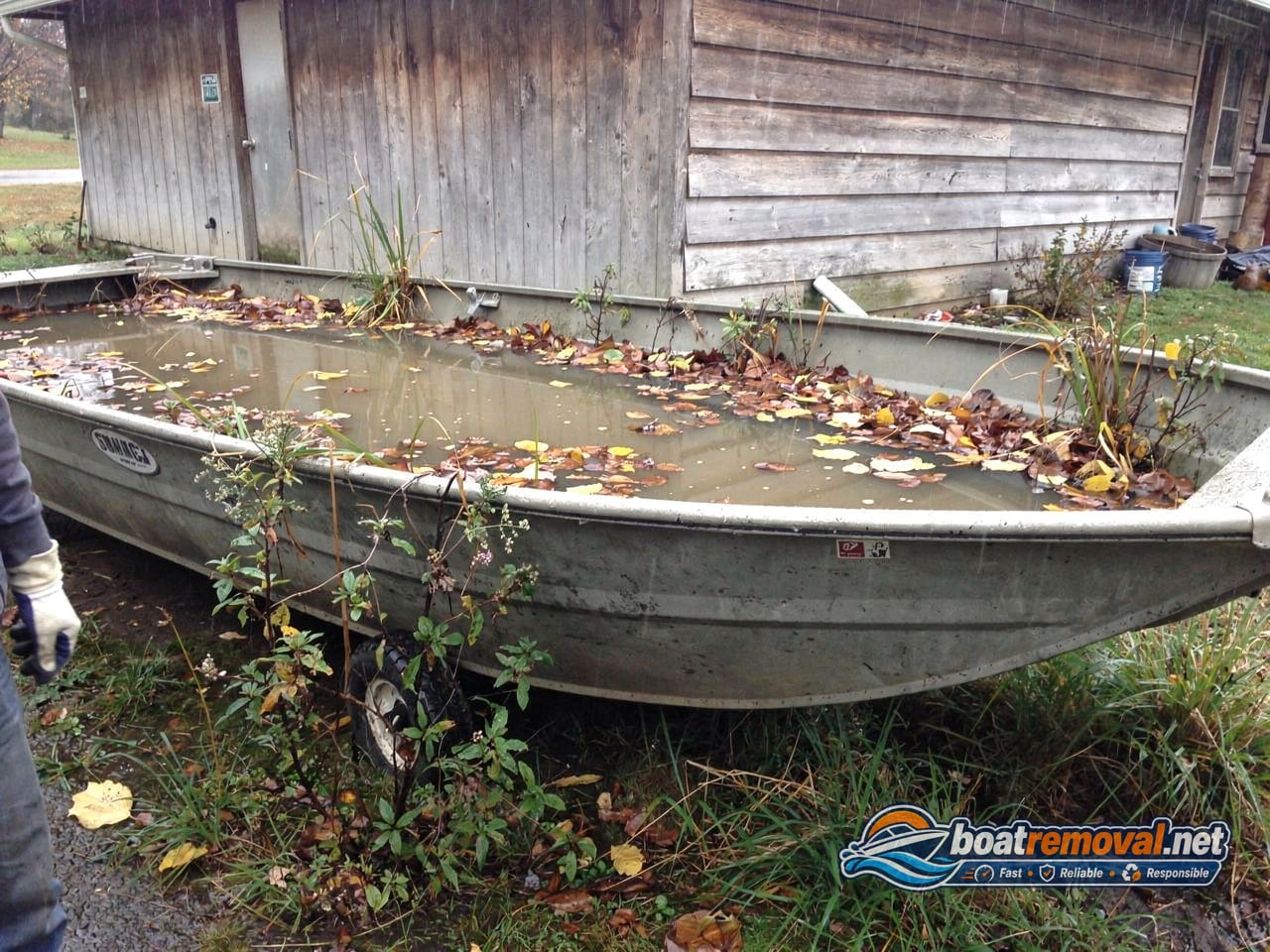 junk boat removal, 16 ft aluminum fishing boat abandoned by a garage