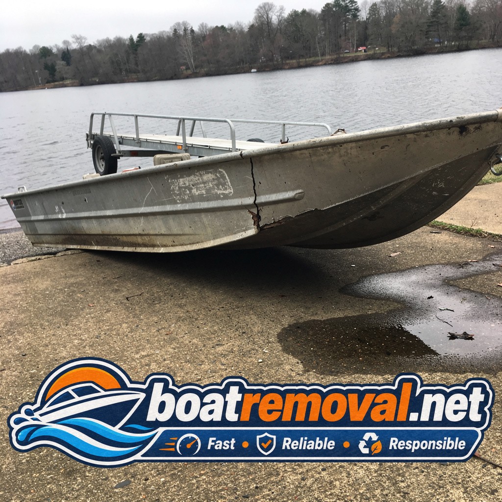 Aluminum fishing boat with a cracked hull seam resting near a lake boat ramp