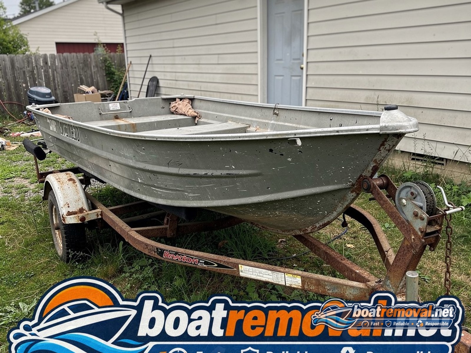 Small aluminum fishing boat with rusted trailer bunks sitting behind a house