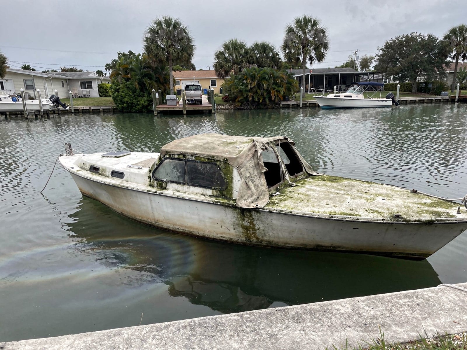 Sunken boat recovery in Gibsonton, FL: before Sunken 26 ft MacGregor 26 in a canal by the seawall in Gibsonton, FL