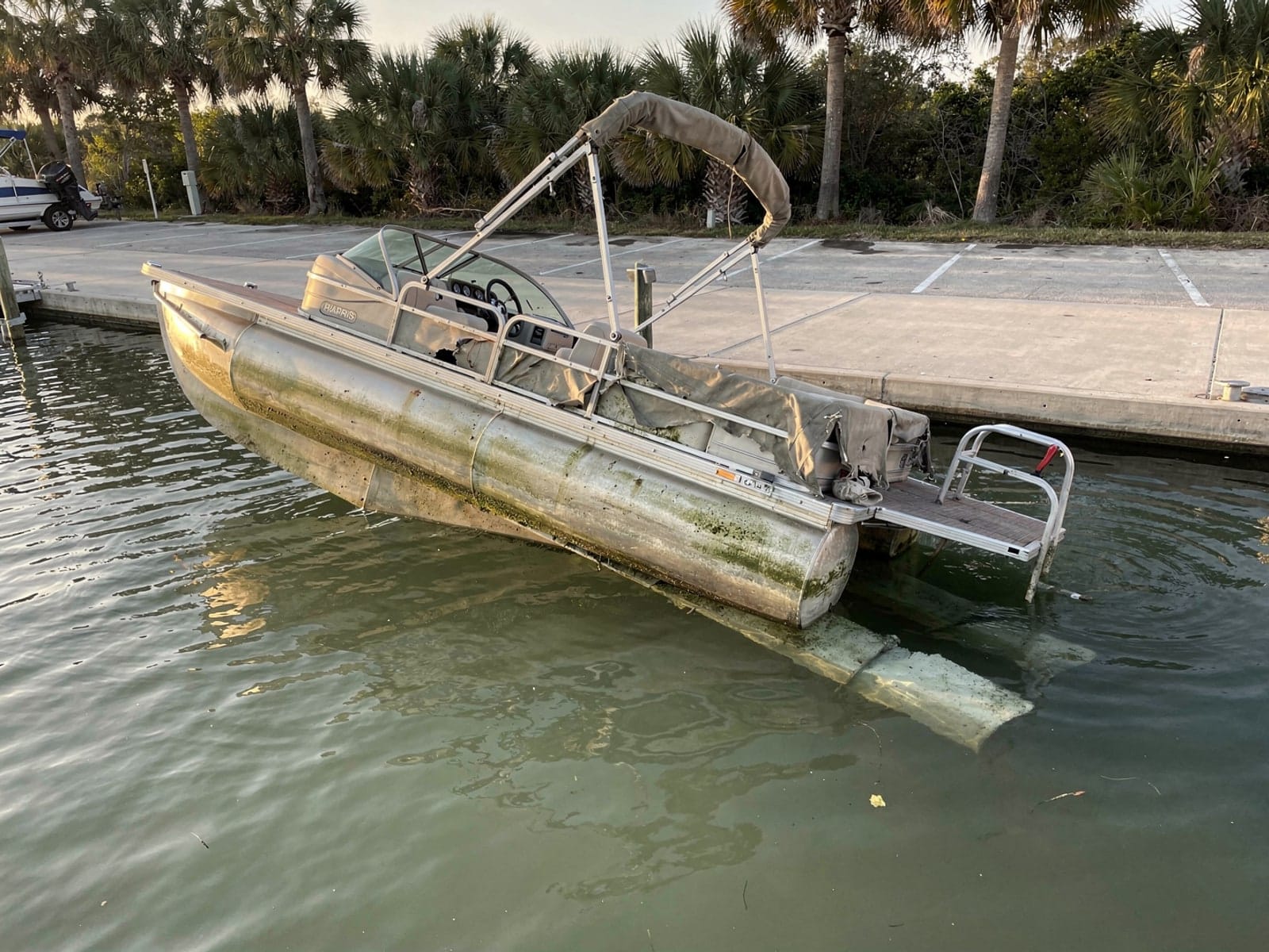 Sunken boat recovery in Holiday, FL: before Sunken 24 ft Harris FloteBote 24 by a boat ramp in Holiday, FL