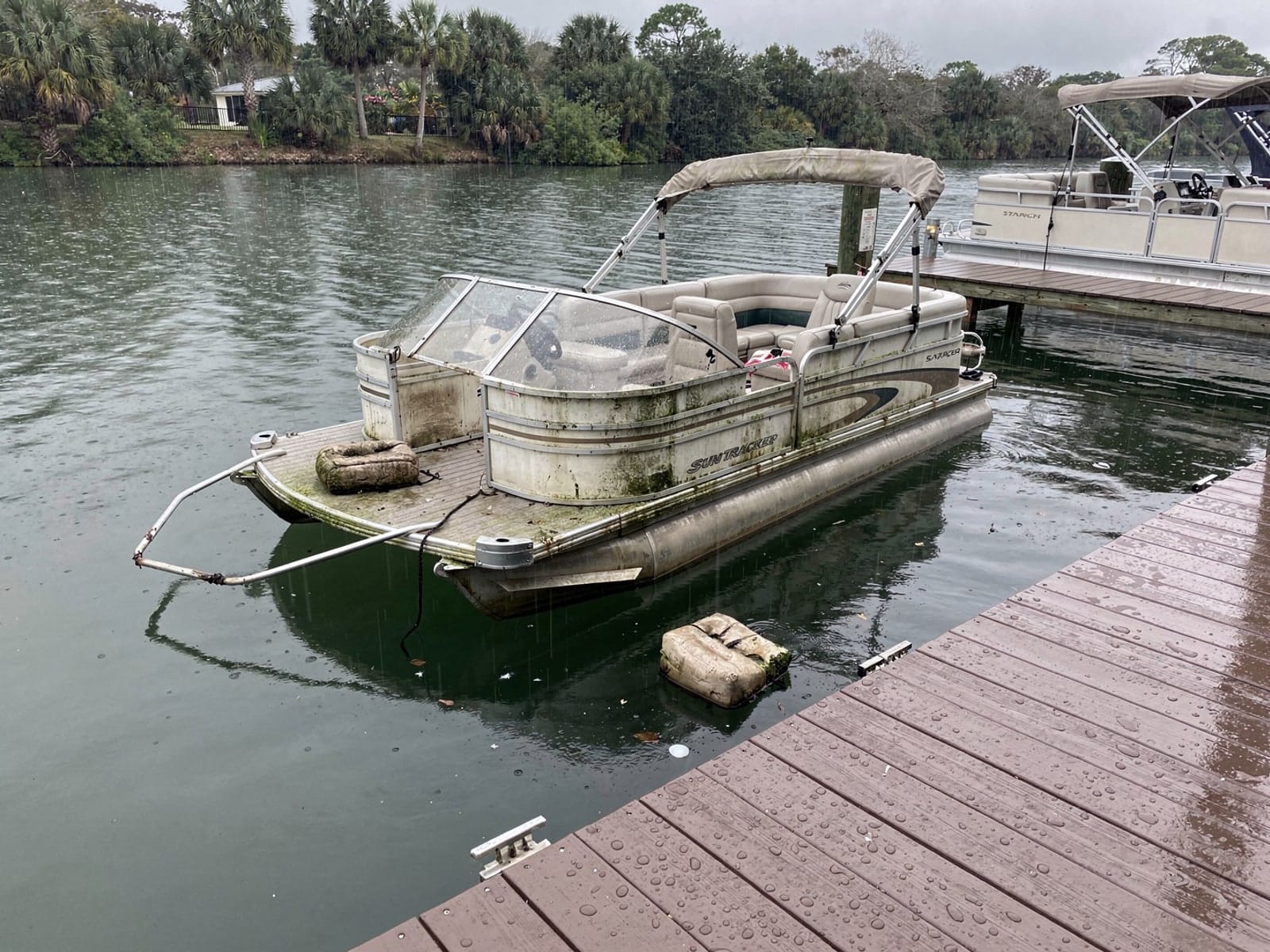 Sunken boat recovery in Lealman, FL: before Sunken 22 ft Sun Tracker Party Barge 22 at a lake dock in Lealman, FL