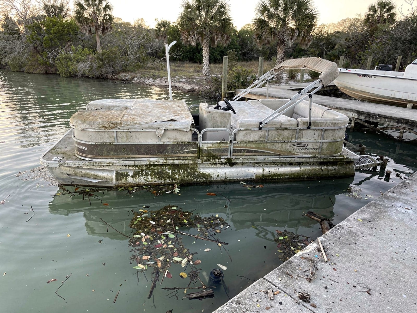 Sunken boat recovery in North Lauderdale, FL: before Sunken 24 ft Harris FloteBote 24 by a boat ramp in North Lauderdale, FL