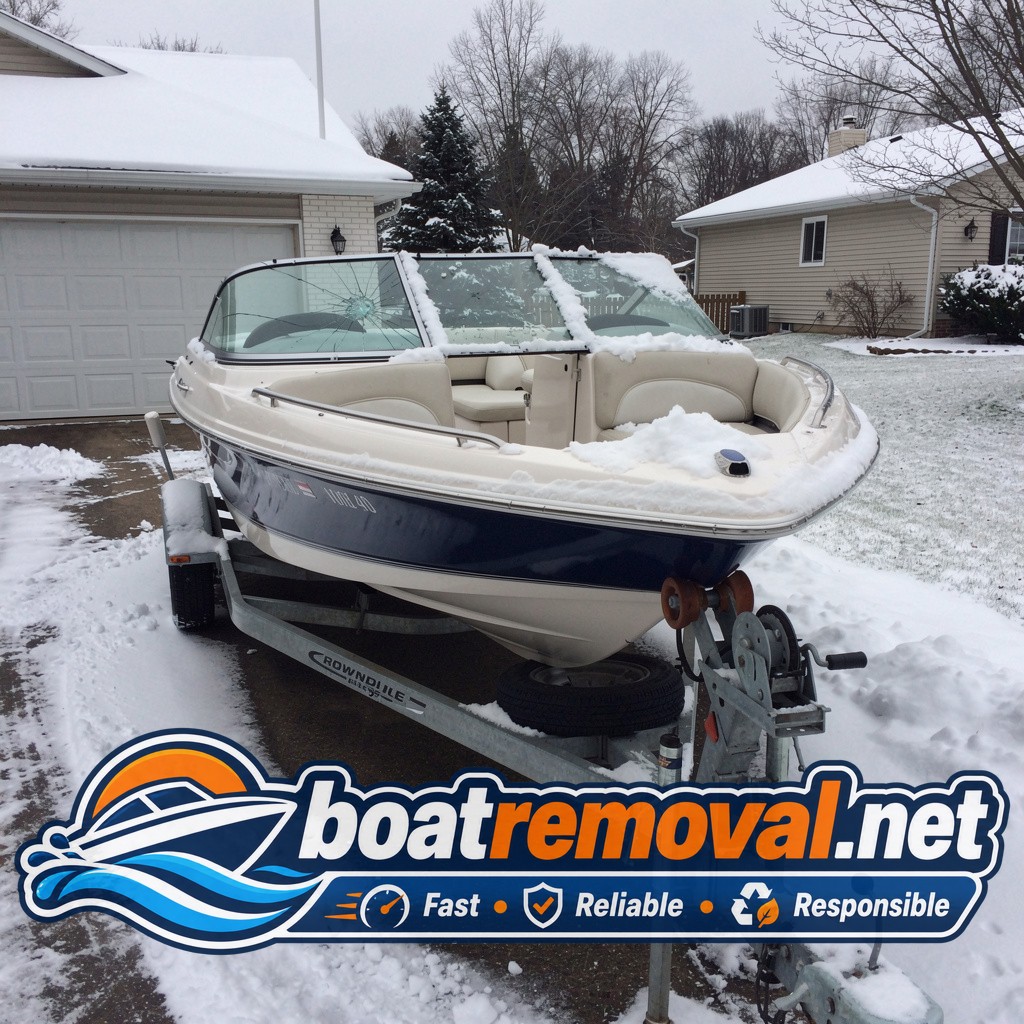 Mid-size bowrider boat with a cracked windshield sitting on a trailer under snow