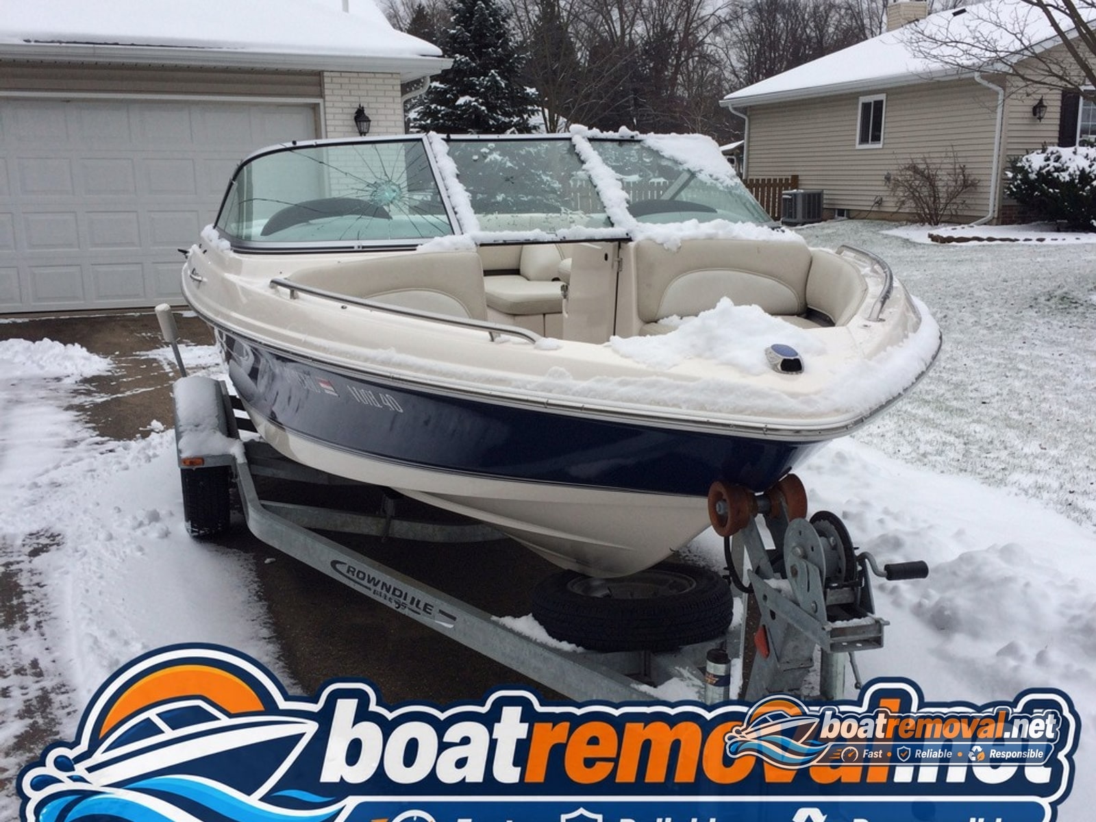 Mid-size bowrider boat with a cracked windshield sitting on a trailer under snow