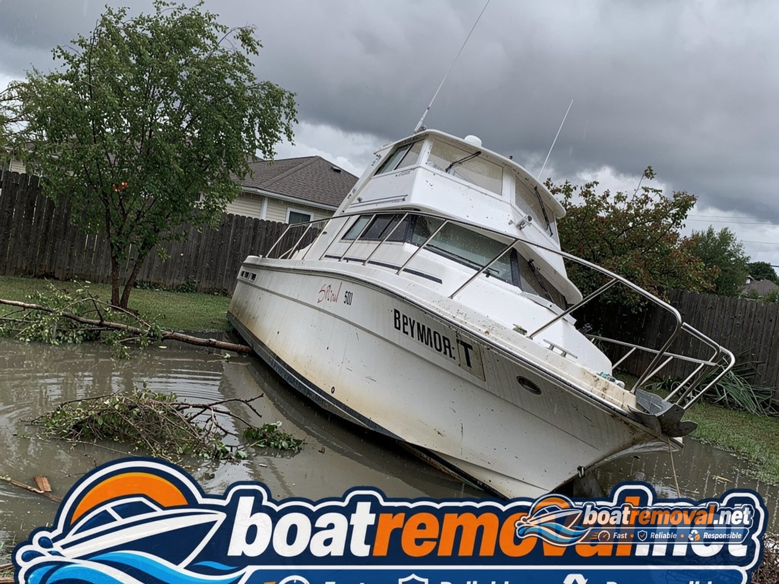 Large cabin cruiser boat tipped on its side in a flooded yard after a storm