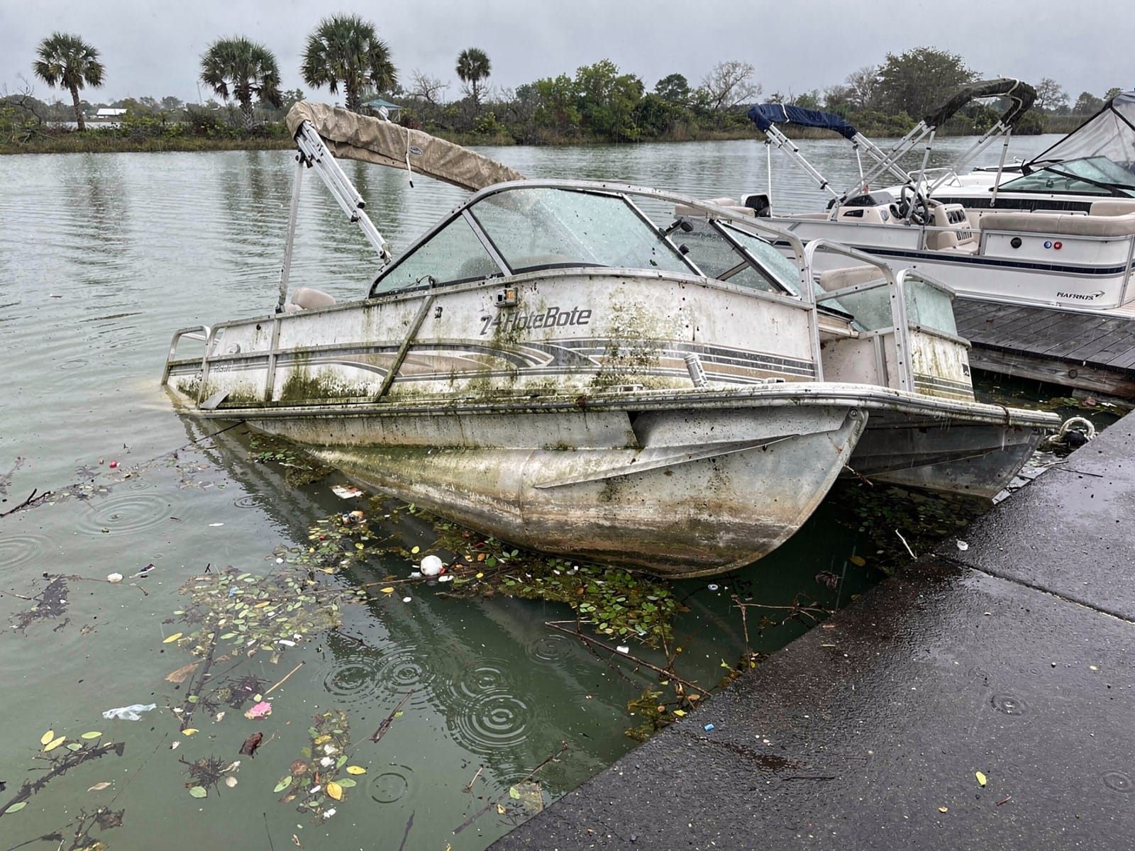 Sunken boat recovery in Port Charlotte, FL: before Sunken 24 ft Harris FloteBote 24 by a boat ramp in Port Charlotte, FL
