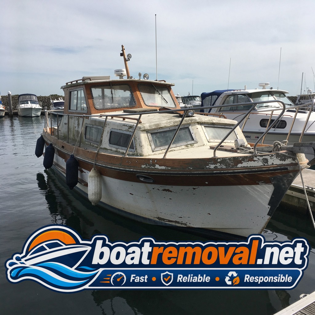 Older cabin cruiser boat with peeling varnish tied up in a marina slip