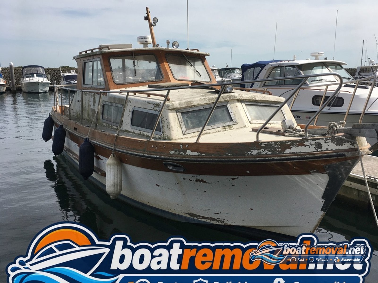 Older cabin cruiser boat with peeling varnish tied up in a marina slip