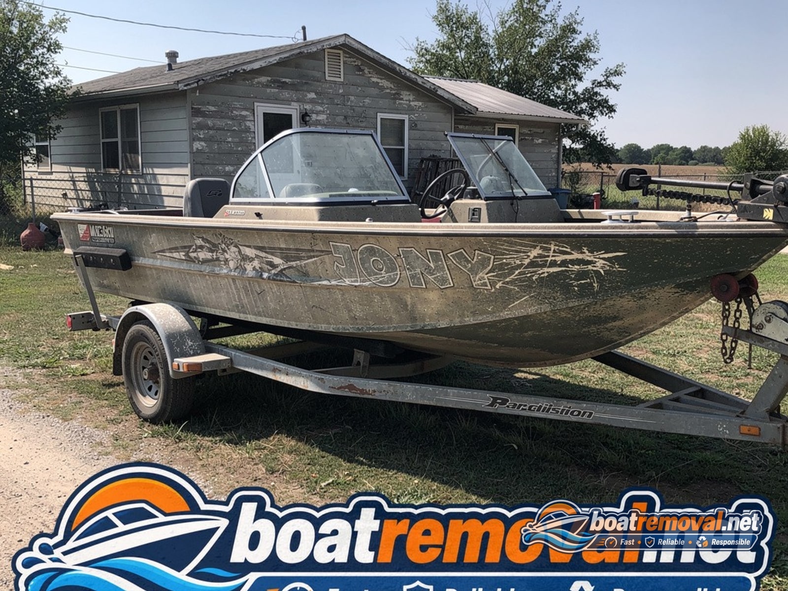 Bass boat with faded graphics sitting on a trailer near a rural house
