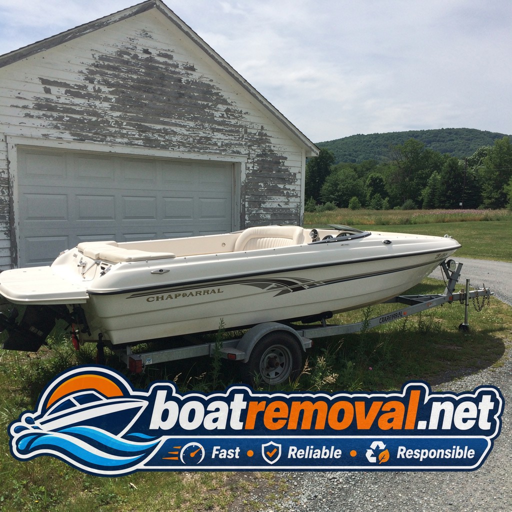 Mid-size bowrider boat on a trailer parked beside a garage with peeling paint