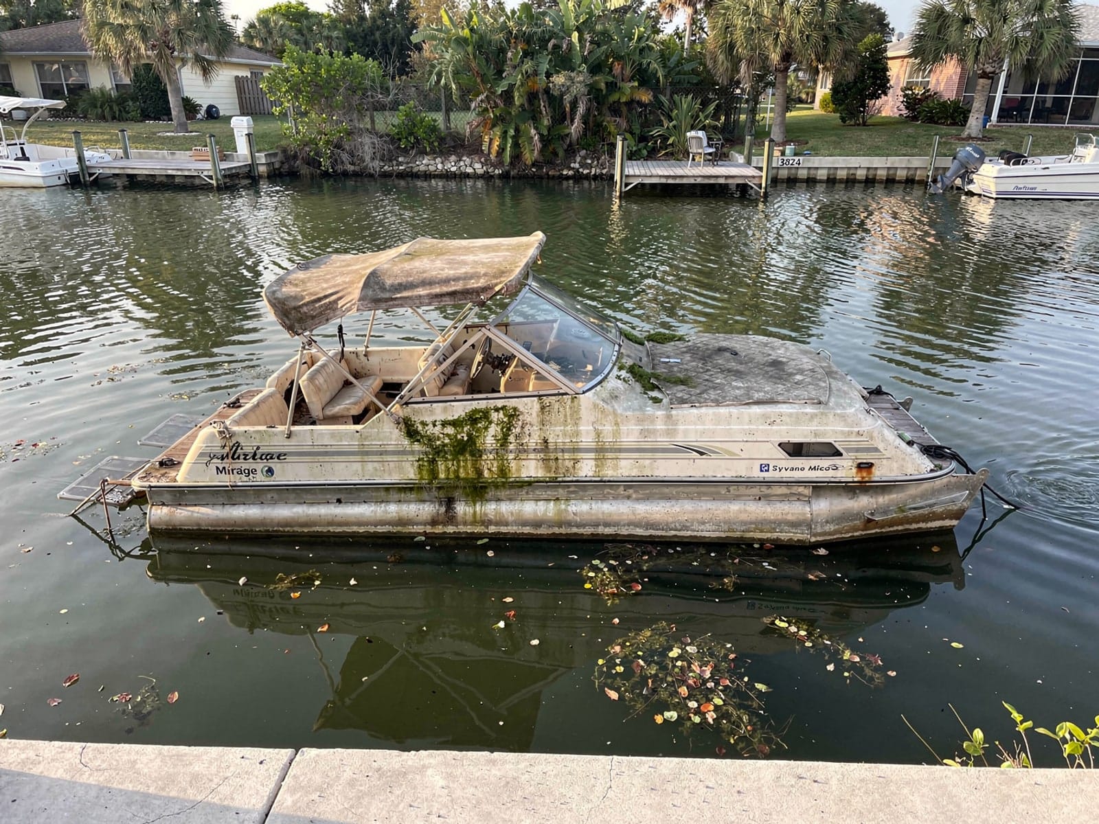 Sunken boat recovery in Pebble Creek, FL: before Sunken 20 ft Sylvan Mirage 20 in a canal by the seawall in Pebble Creek, FL