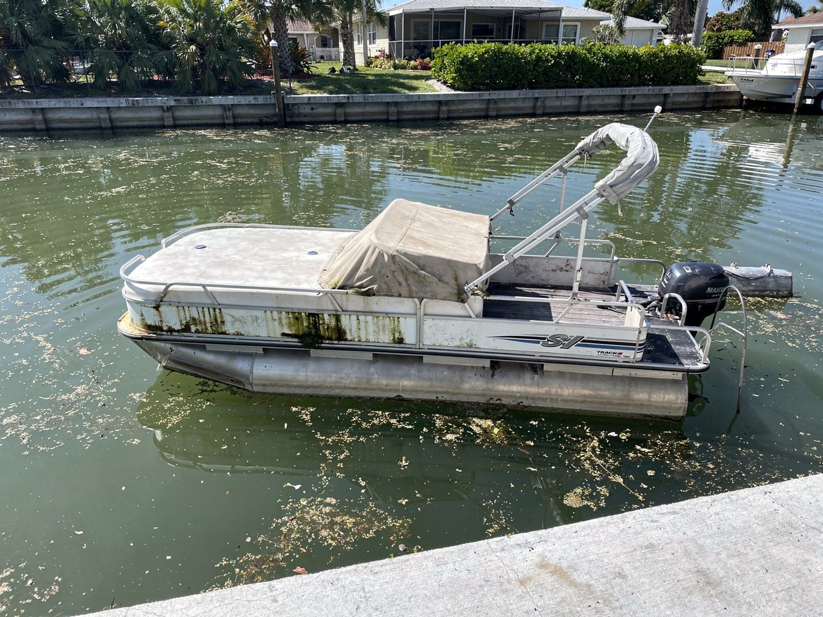Sunken boat recovery in Largo, FL: before Sunken 22 ft Sun Tracker Party Barge 22 in a canal by the seawall in Largo, FL