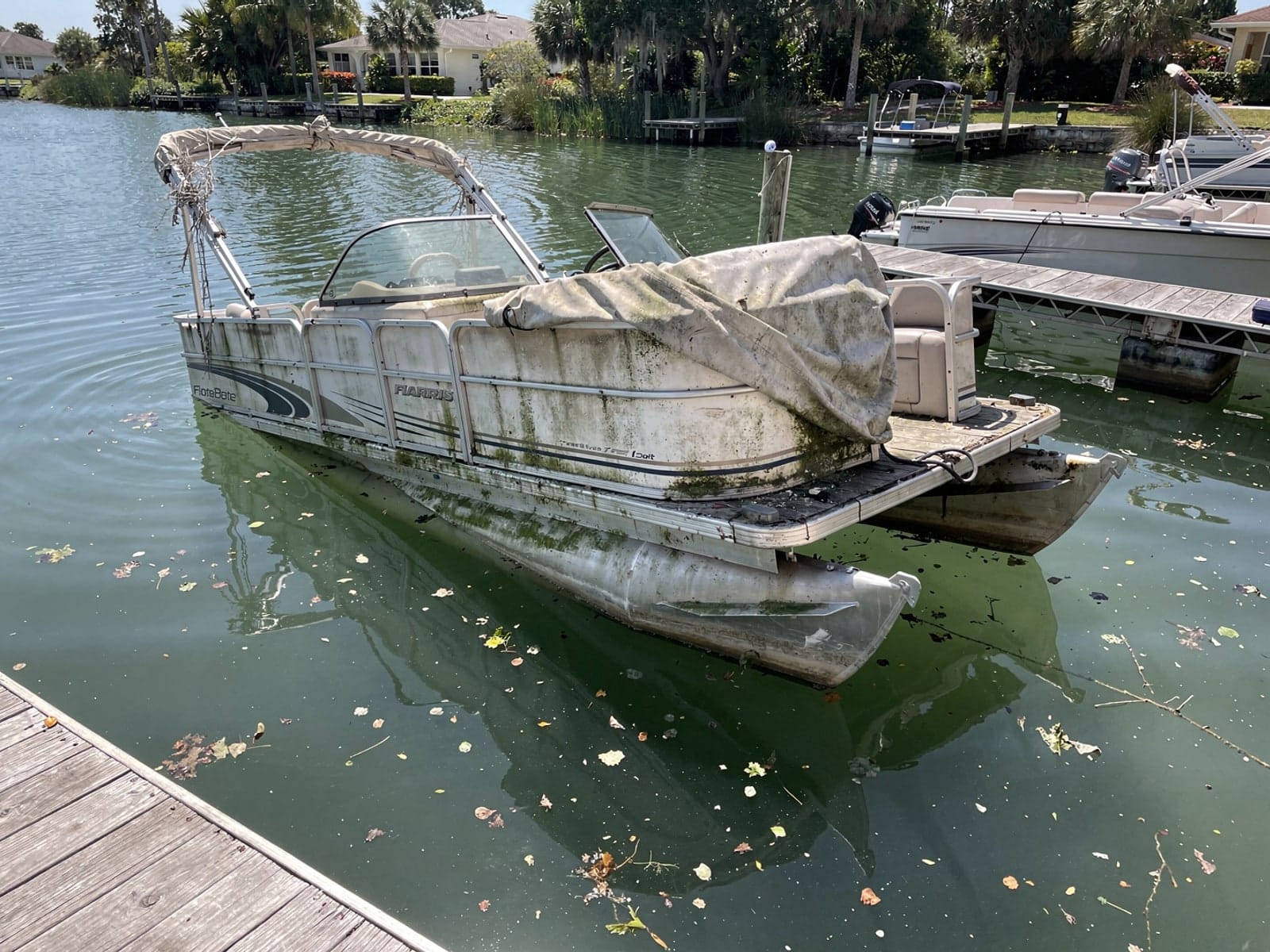 Sunken boat recovery in Clermont, FL: before Sunken 24 ft Harris FloteBote 24 at a lake dock in Clermont, FL