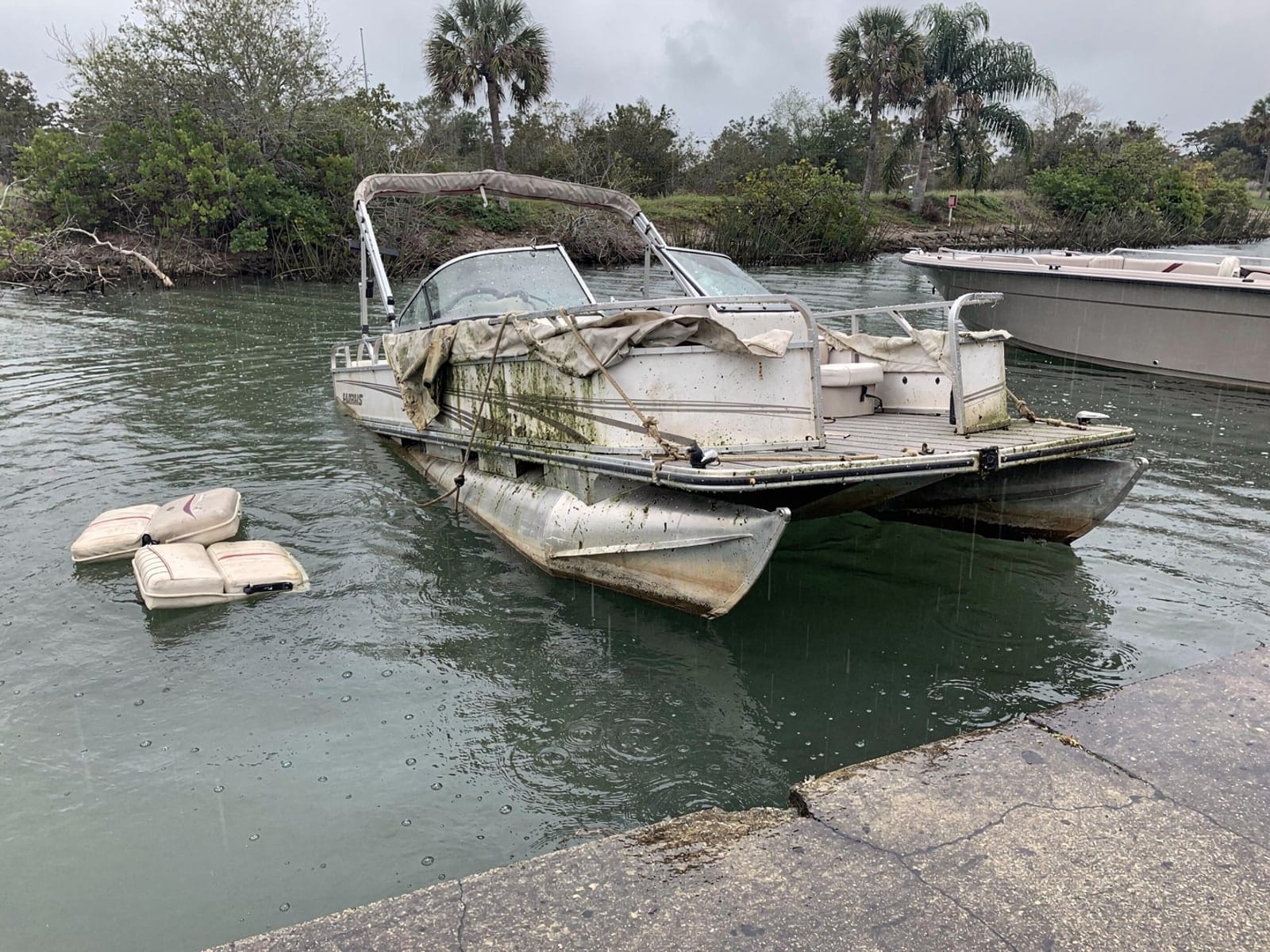 Sunken boat recovery in Fort Myers, FL: before Sunken 24 ft Harris FloteBote 24 by a boat ramp in Fort Myers, FL