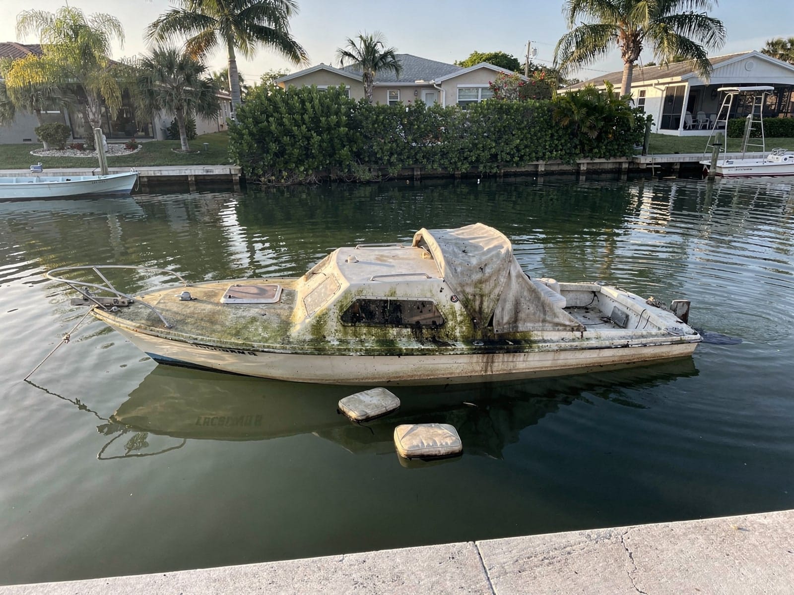 Sunken boat recovery in Country Club, FL: before Sunken 26 ft MacGregor 26 in a canal by the seawall in Country Club, FL