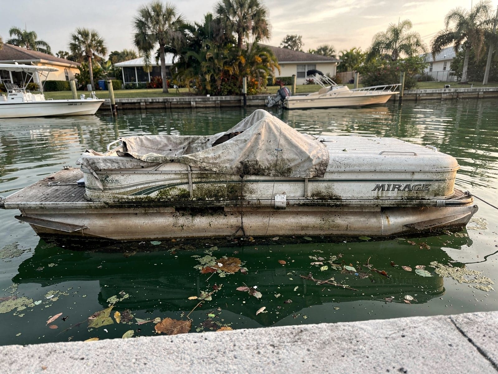 Sunken boat recovery in Port St Lucie, FL: before Sunken 20 ft Sylvan Mirage 20 in a canal by the seawall in Port St Lucie, FL