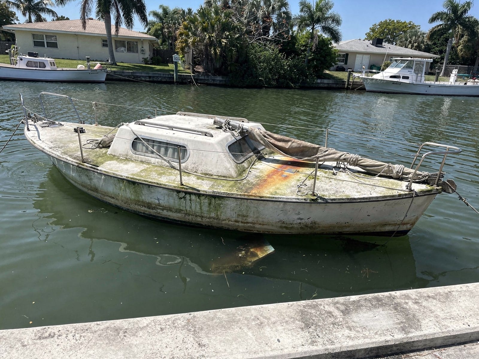 Sunken boat recovery in Vero Beach South, FL: before Sunken 22 ft Catalina 22 in a canal by the seawall in Vero Beach South, FL